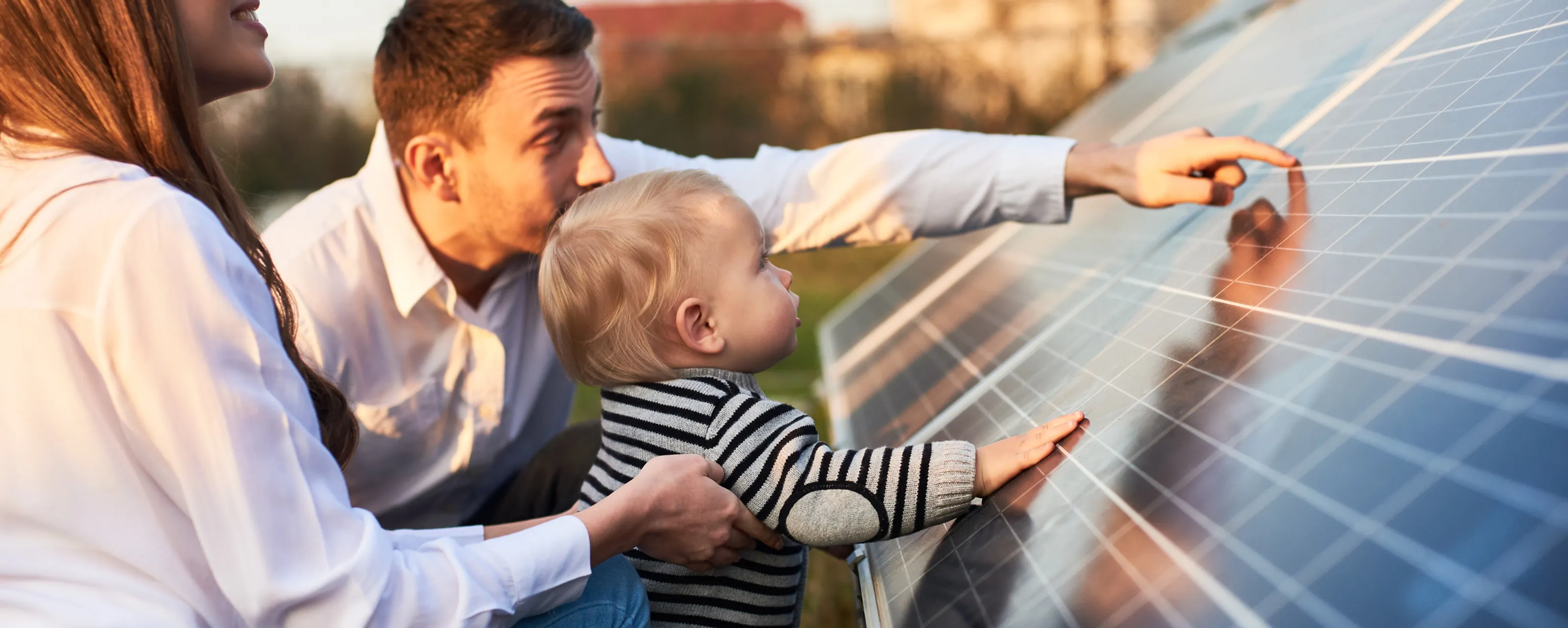 Familie på tre studerer solcellepanel på nært hold ved solnedgang