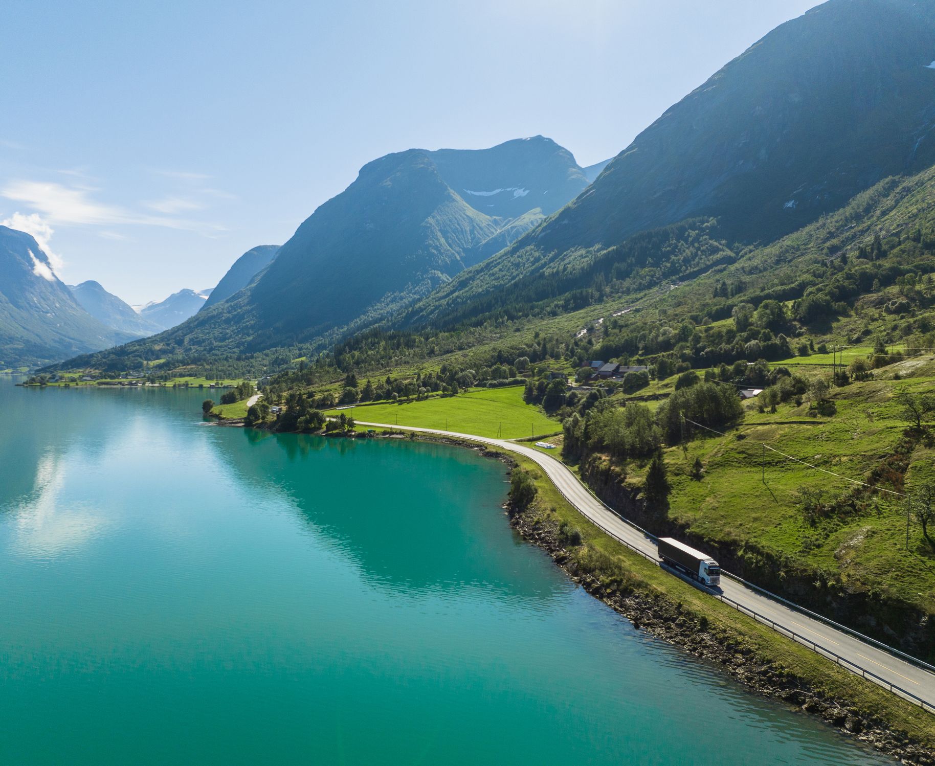 En lastebil kjører langs en idyllisk norsk fjord, med bratte fjell rundt