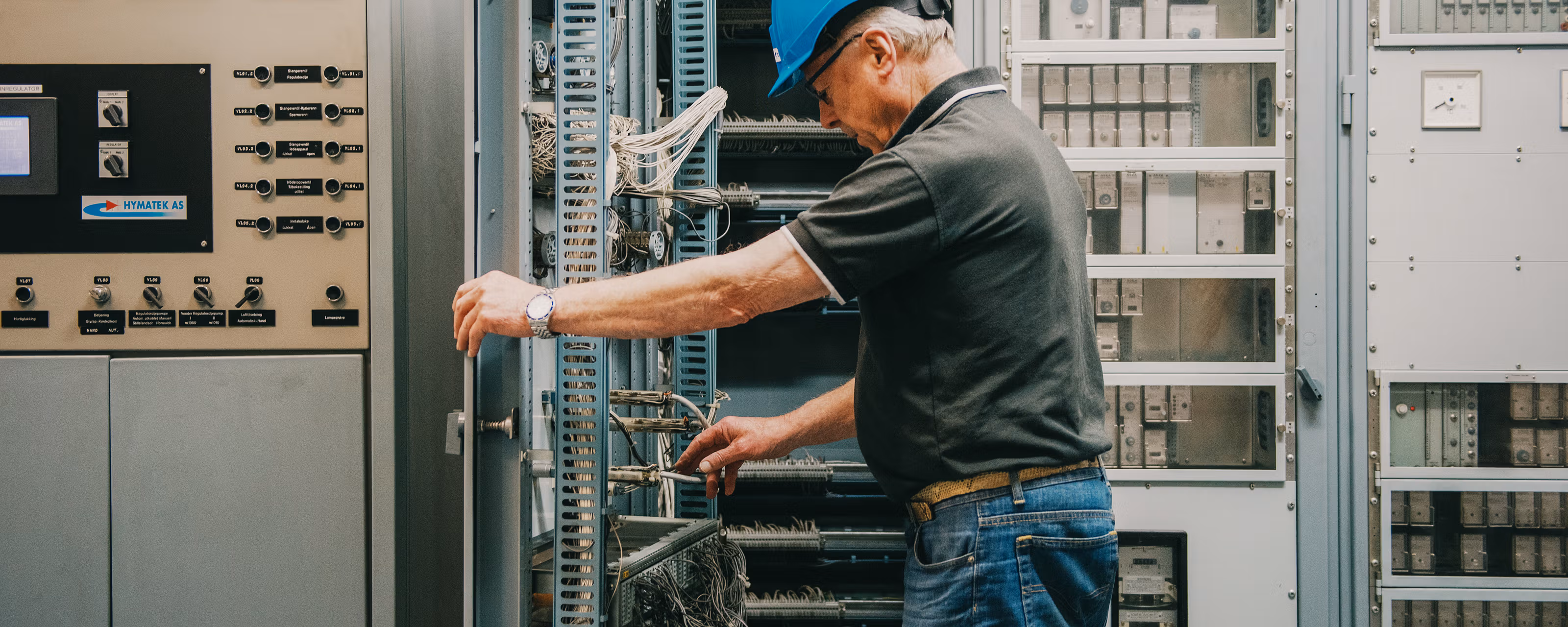 En mann med blå hjelm har åpnet et skap med mange ledninger.