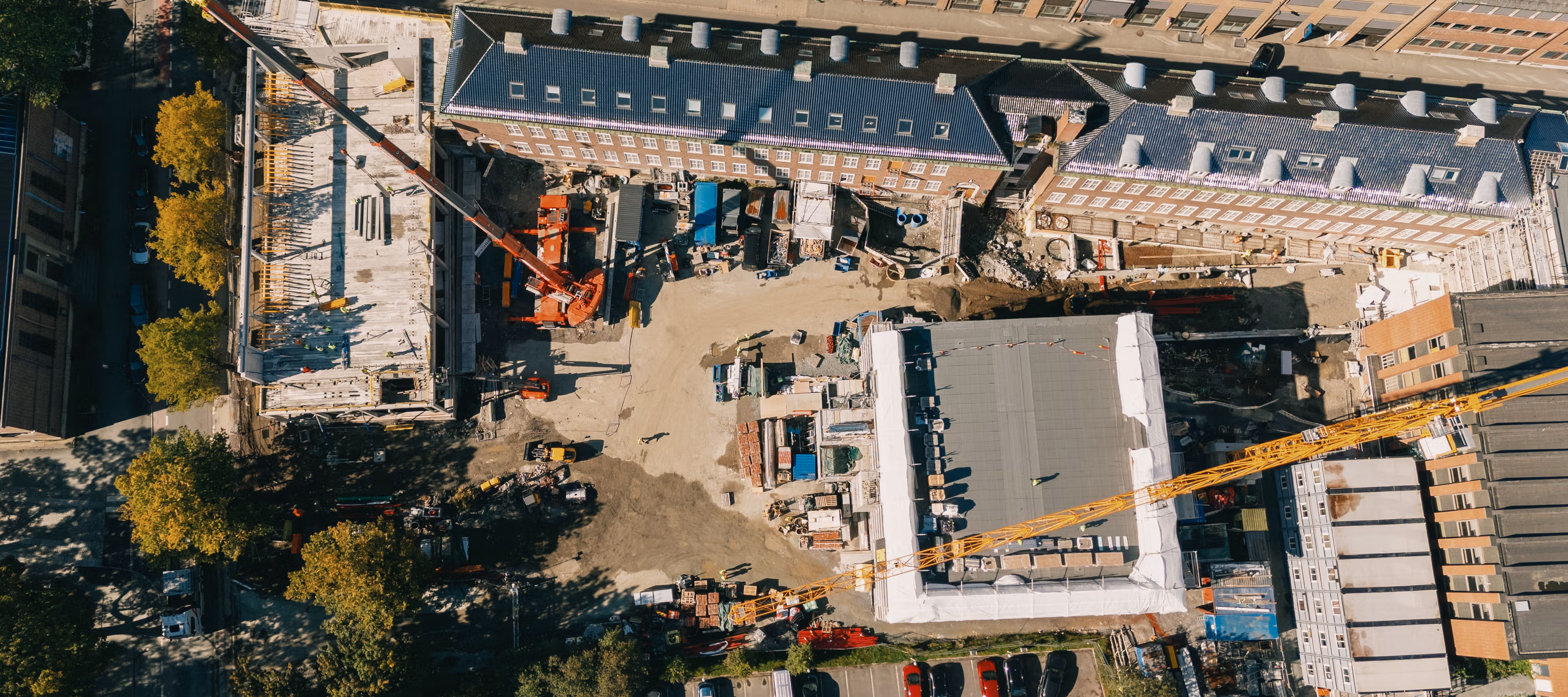 Byggeplass sett rett ovenfra med to heisekraner midt i by-bebyggelse i Trondheim sentrum.