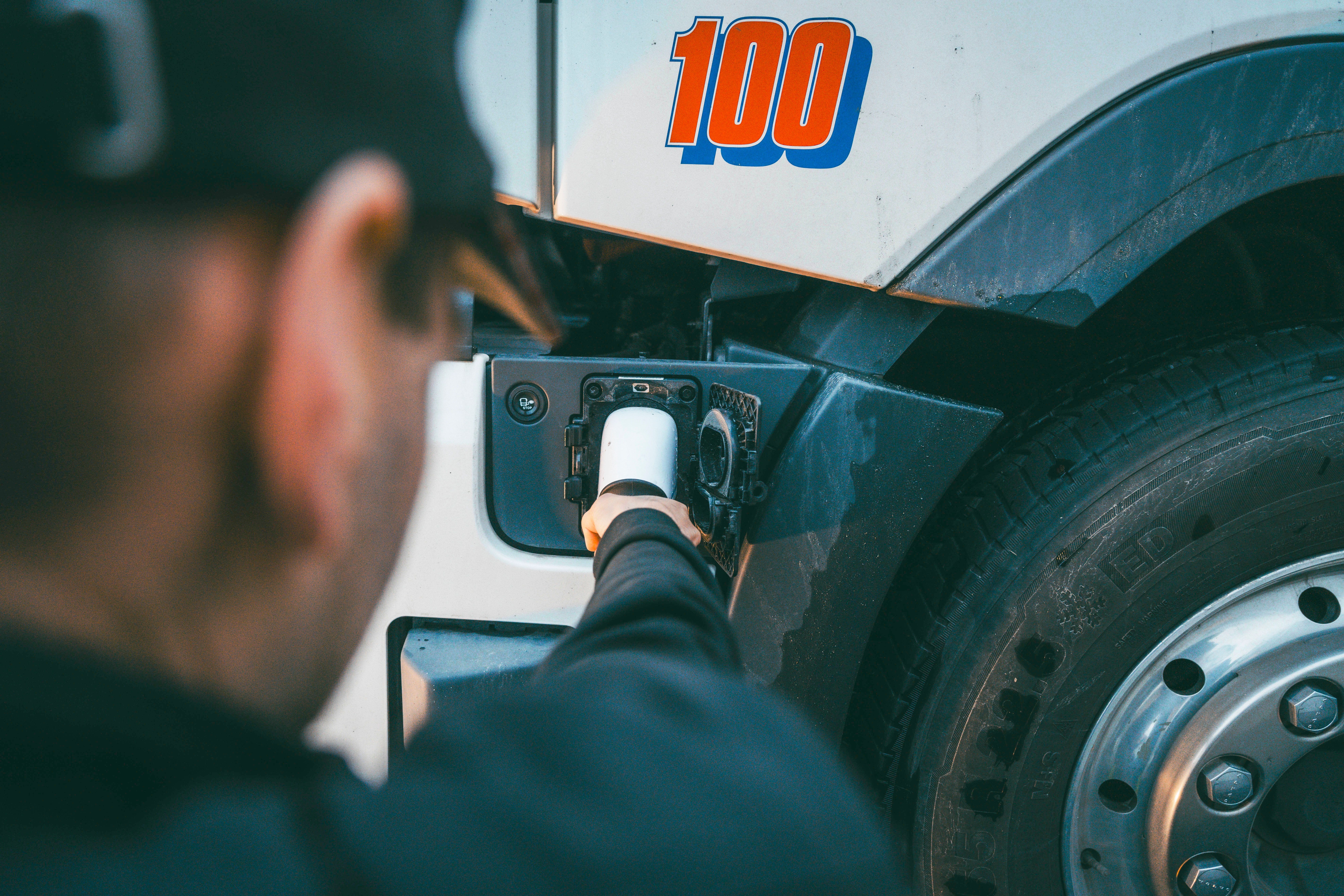 Nærbilde av en mann som holder en ladekabel som føres inn i en elektrisk lastebil.