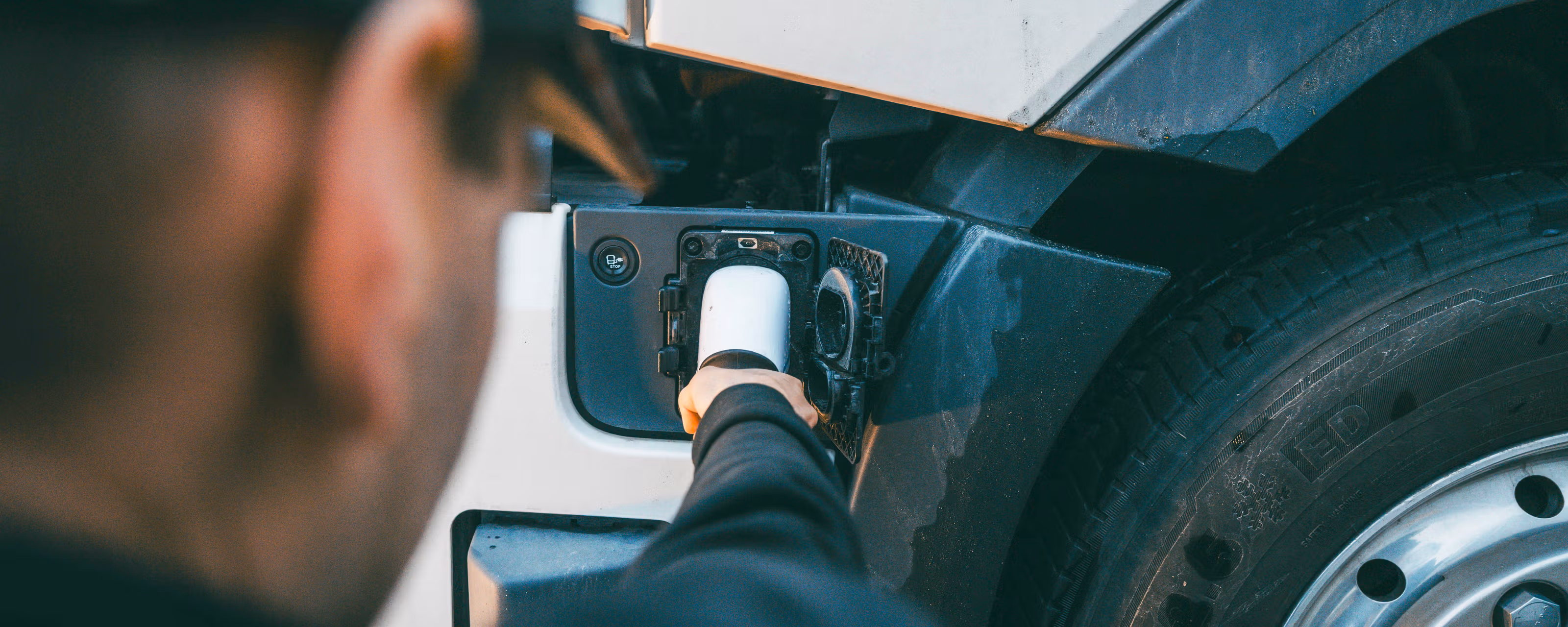 Nærbilde av en mann som holder en ladekabel som føres inn i en elektrisk lastebil.