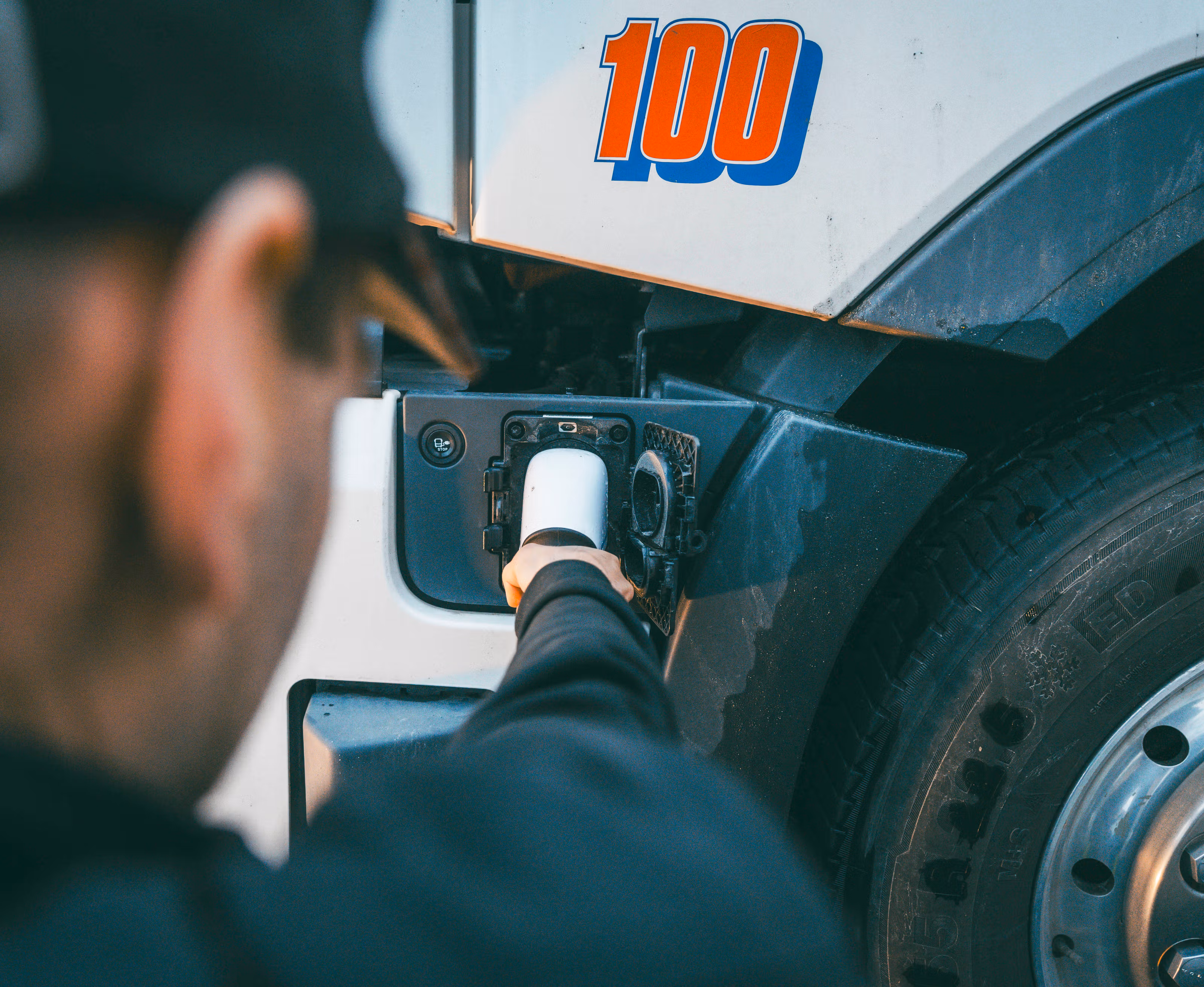 Nærbilde av en mann som holder en ladekabel som føres inn i en elektrisk lastebil.