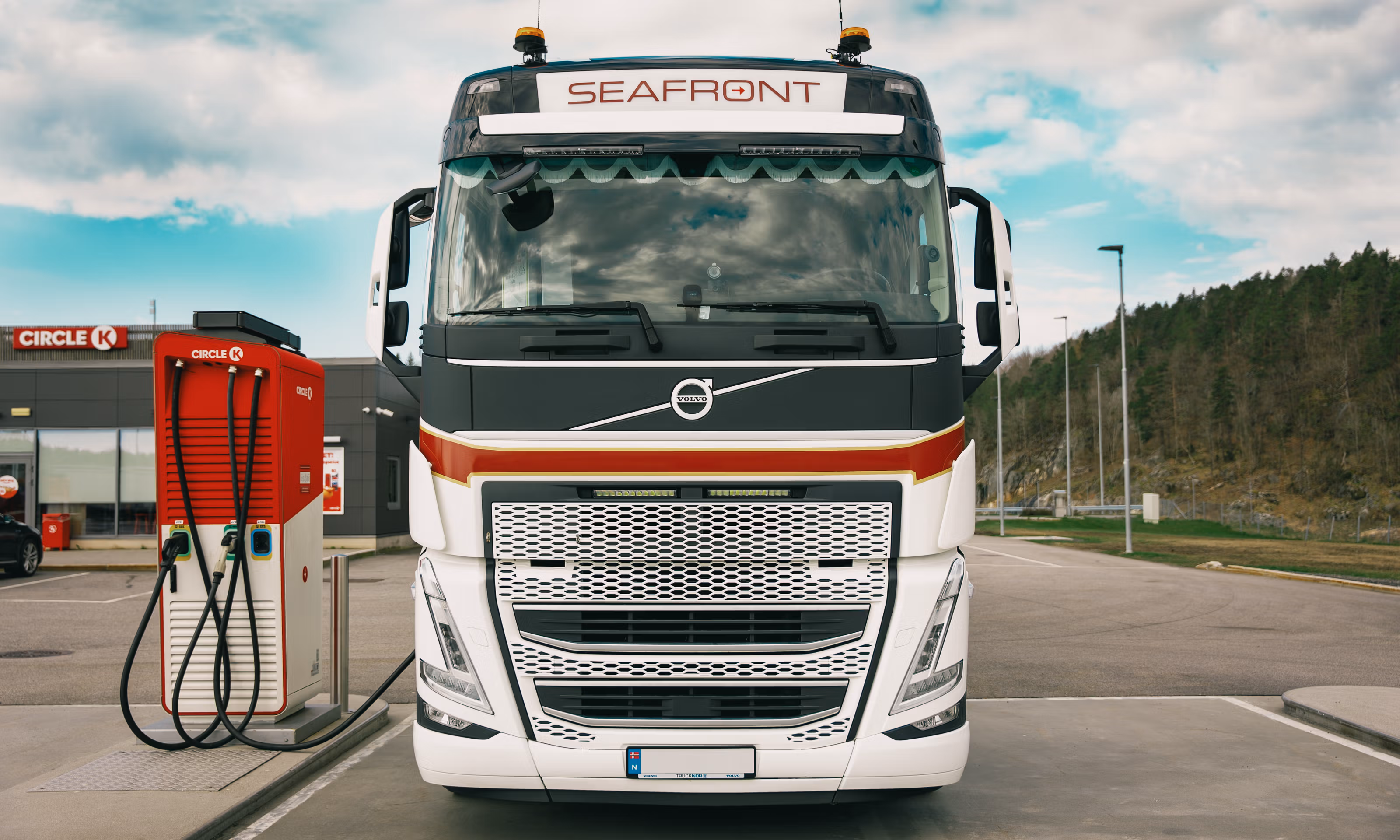 En elektrisk lastebil sett rett forfra på en parkeringsplass, oppstilt ved en rød og hvit lader.