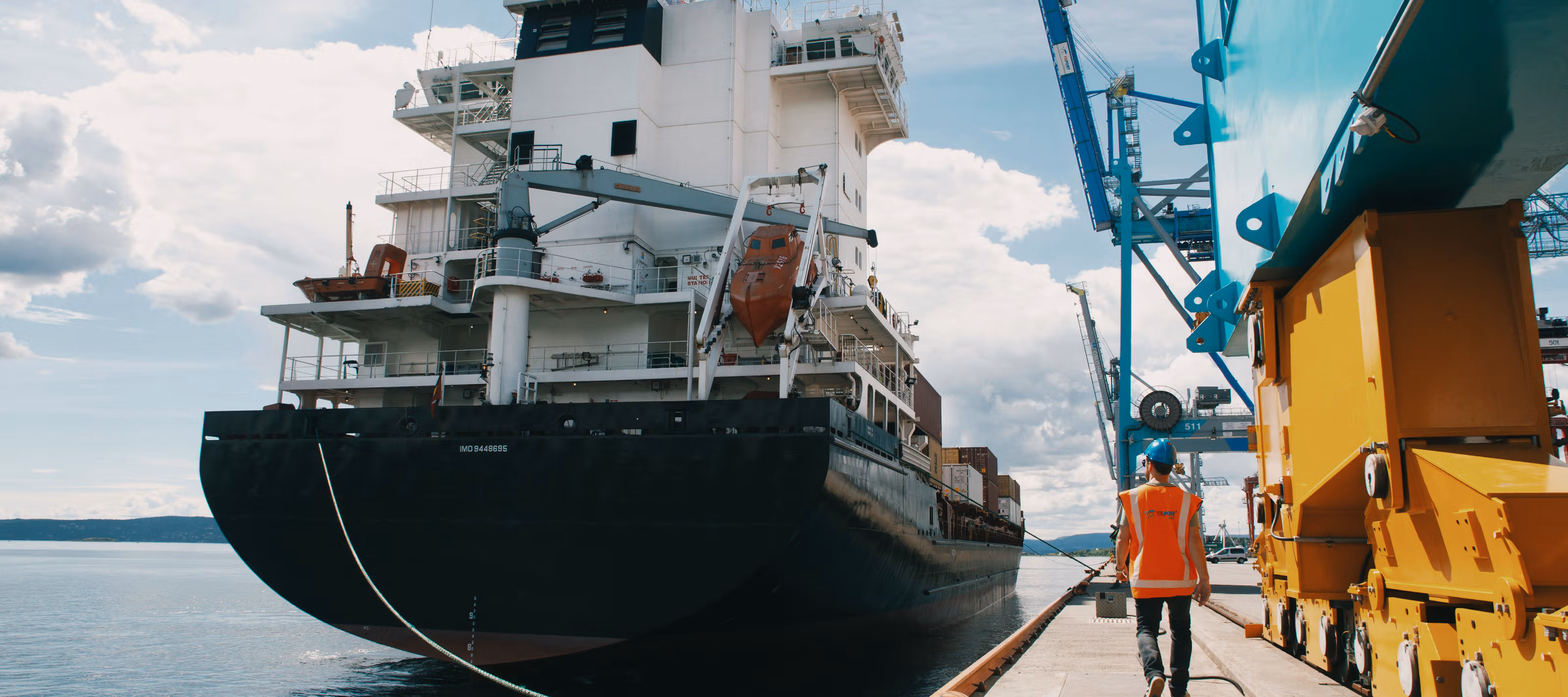 Et skip ligger til kai, med en mann som går med ryggen til.