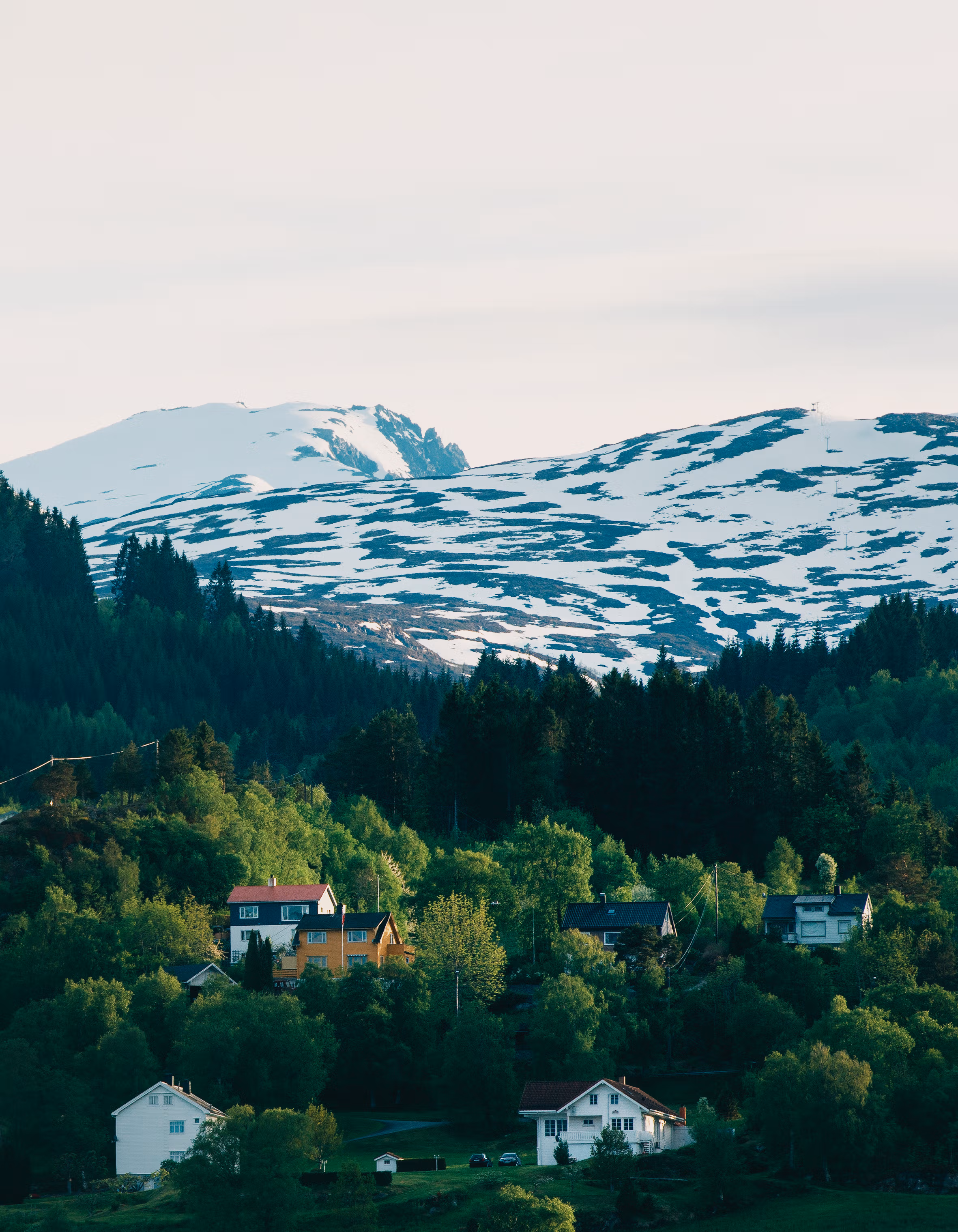 Eneboliger og eldre boliger i et vakkert norsk landskap med snødekte fjell i bakgrunnen.