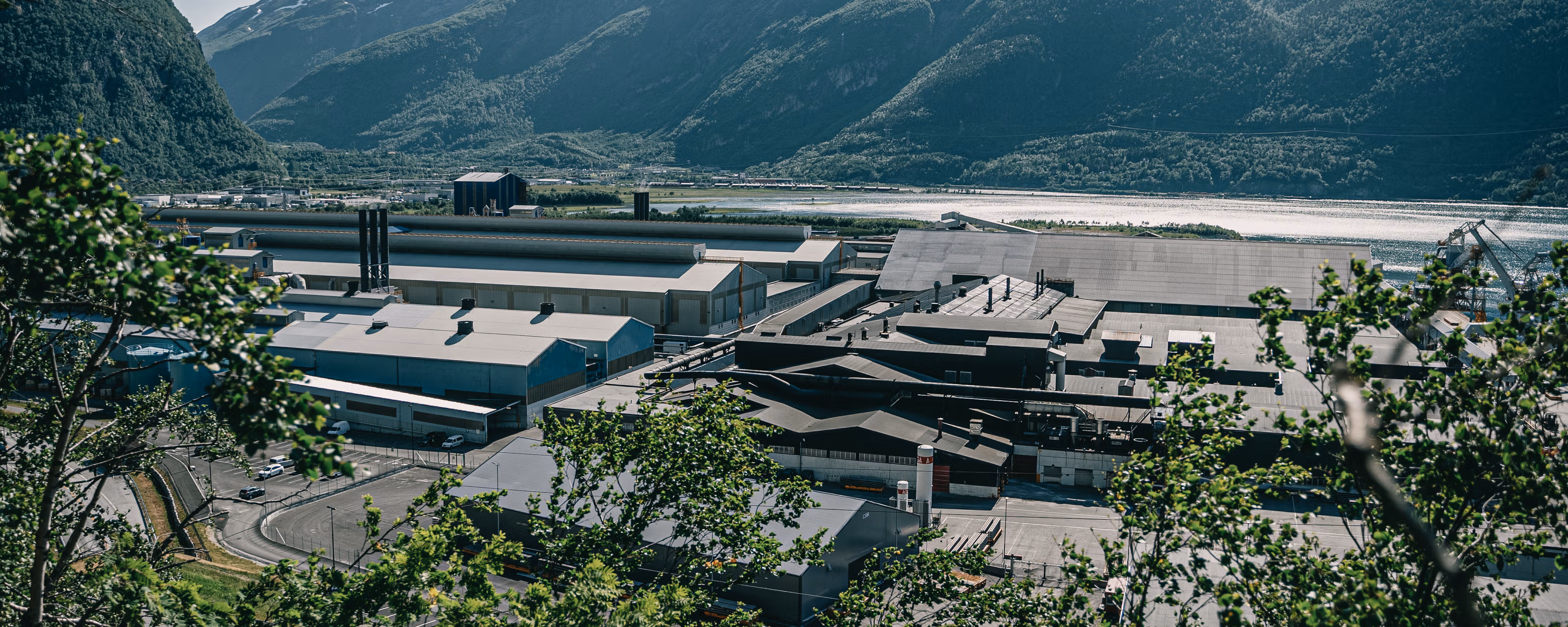 Fabrikken til Norsk Hydro Sunndalsøra med trær i forgrunnen og fjell i bakgrunnen.