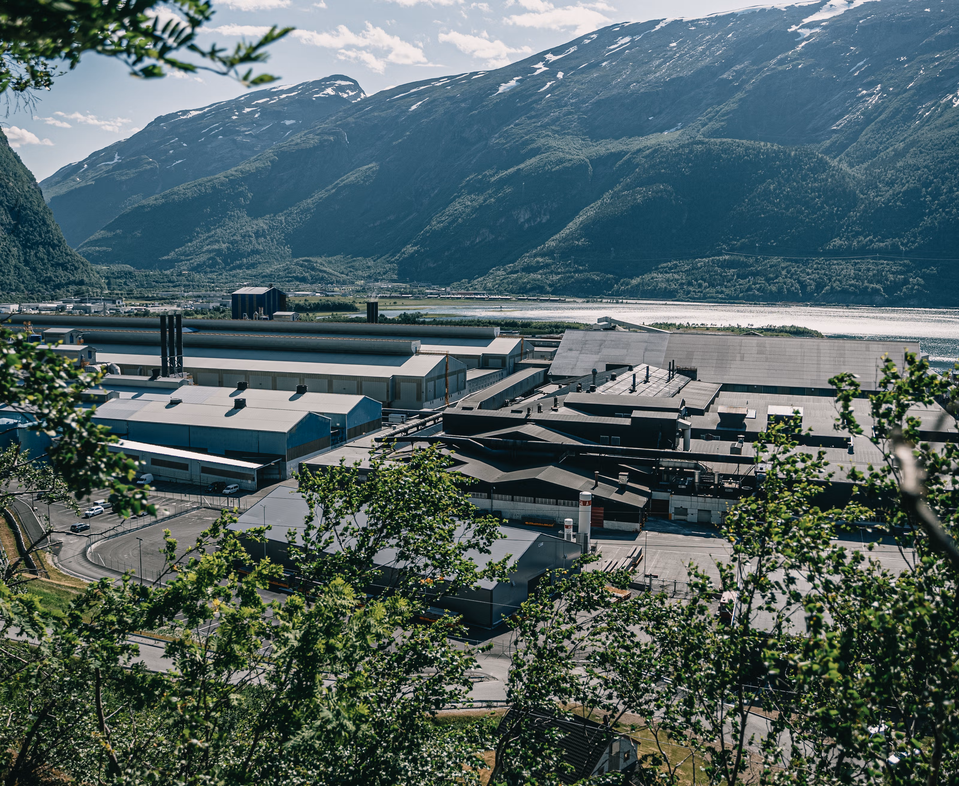 Fabrikken til Norsk Hydro Sunndalsøra med trær i forgrunnen og fjell i bakgrunnen.