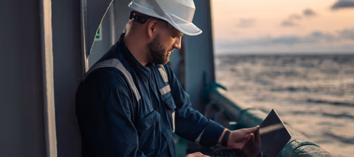 En mann med hjelm ombord i et fartøy mens hans ser på datamaskin.