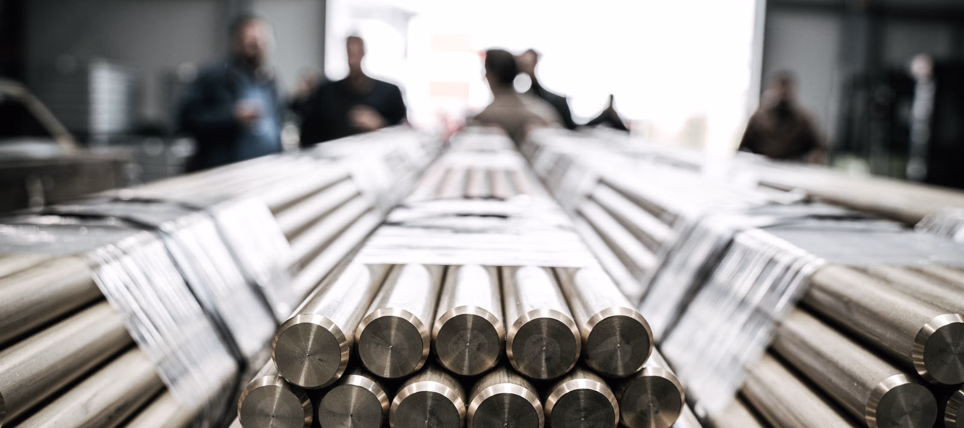 Primæraluminium lagt i store hauger, med arbeidere fra Hydro Sunndal metallverk uskarp i bakgrunnen.