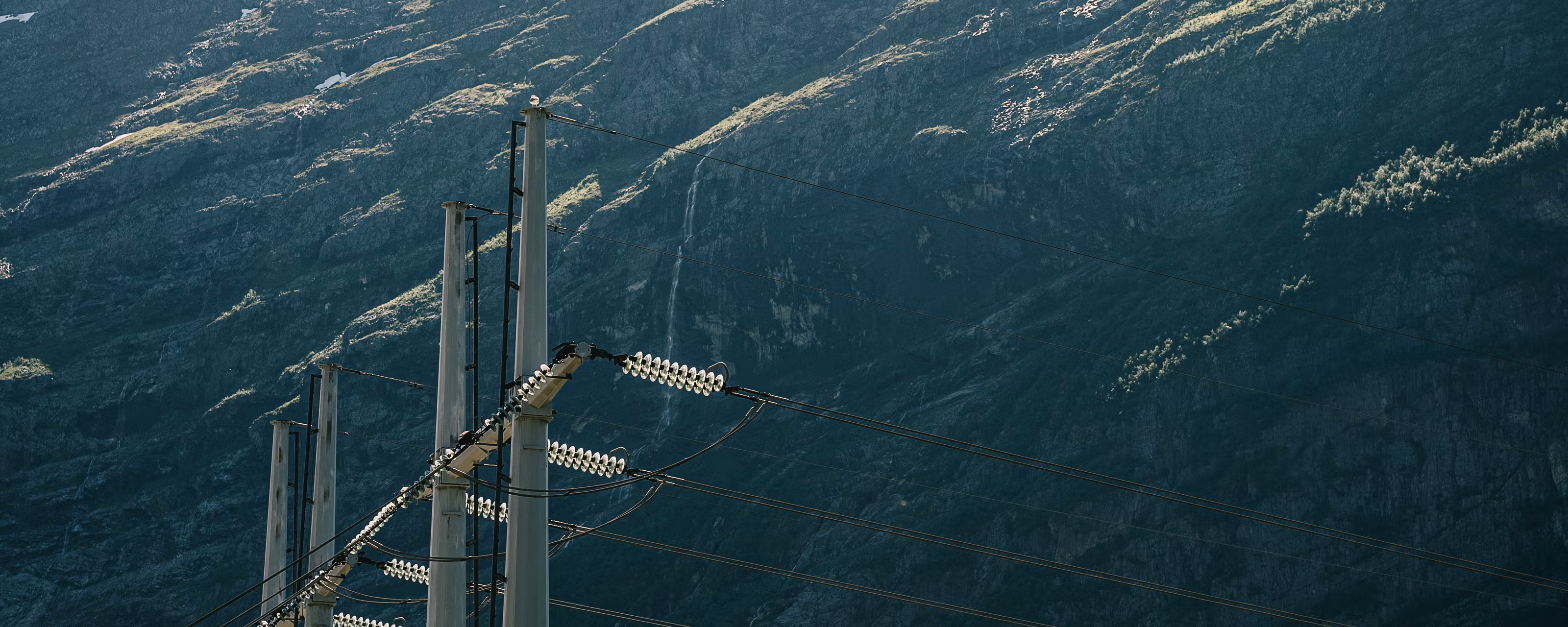 Strømførende kabler i norsk natur med en delvis snødekt fjellside i bakgrunnen.