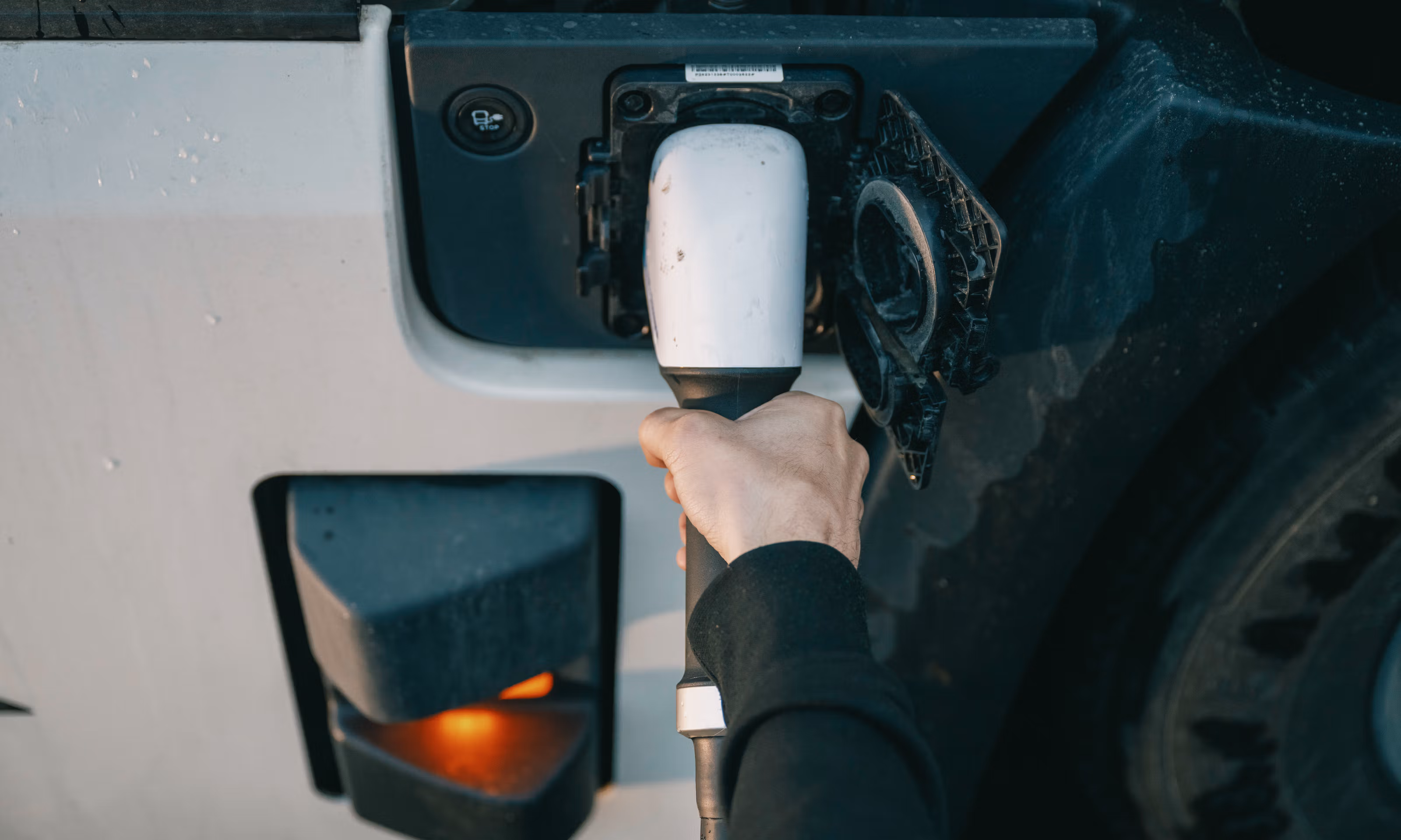 Nærbilde av hånd som stikker laderen i en elektrisk lastebil.