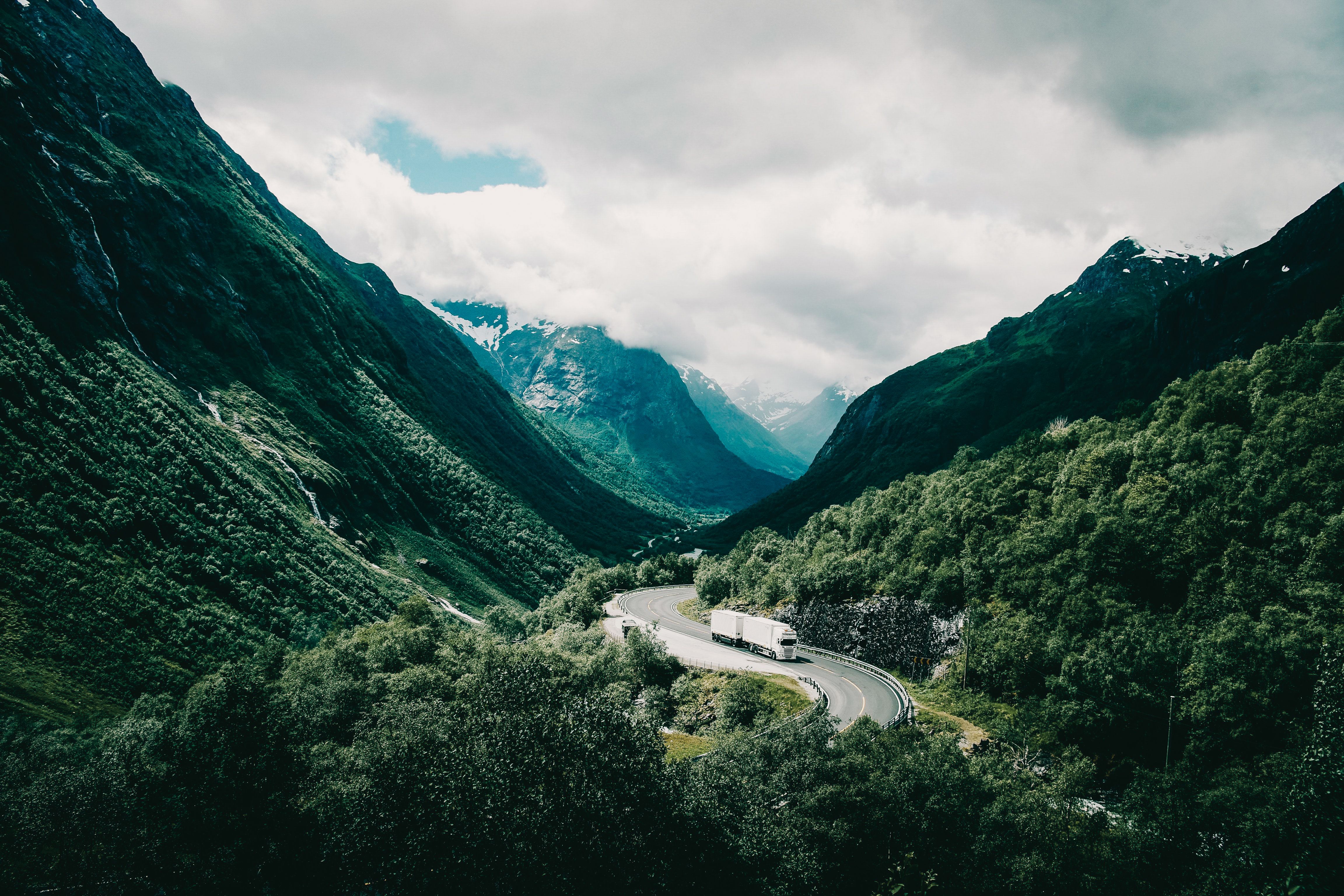 En lastebil som svinger seg igjennom et storslått, grønt, norsk landskap med fjell i bakgrunnen.