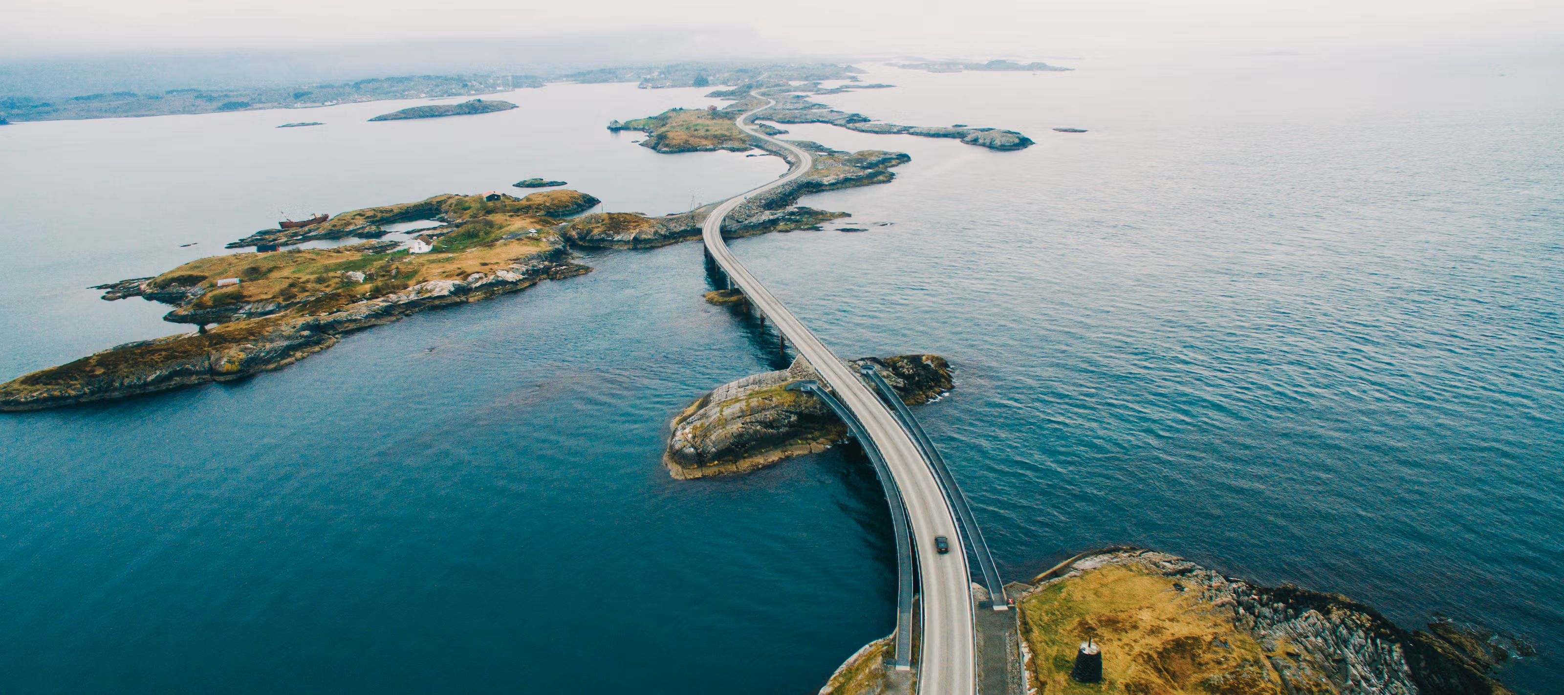 Kjøretøy som befinner seg på en bro som svinger seg igjennom et vakkert norsk kystlandskap.