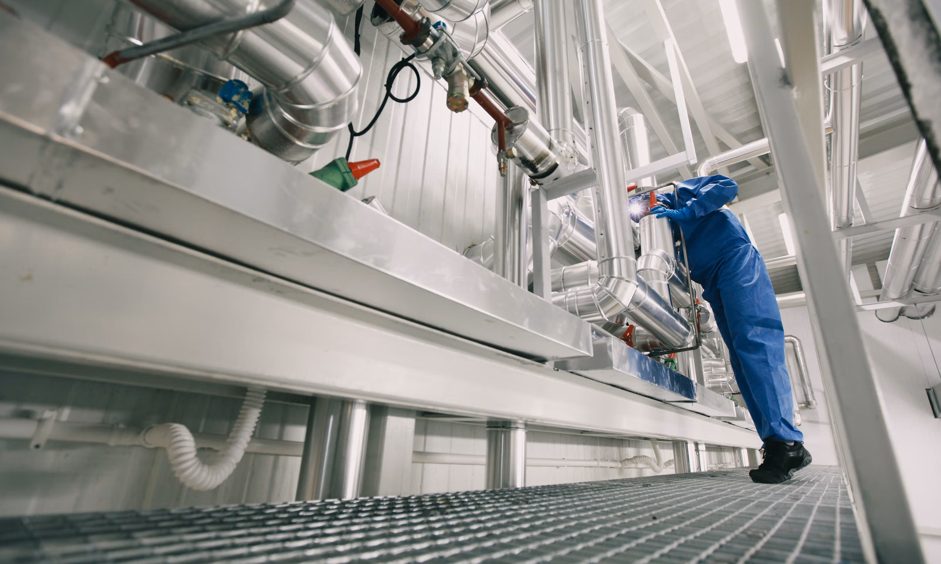 En person i blå våtdrakt befinner seg i et fartøy mens han kikker ned i et rør.