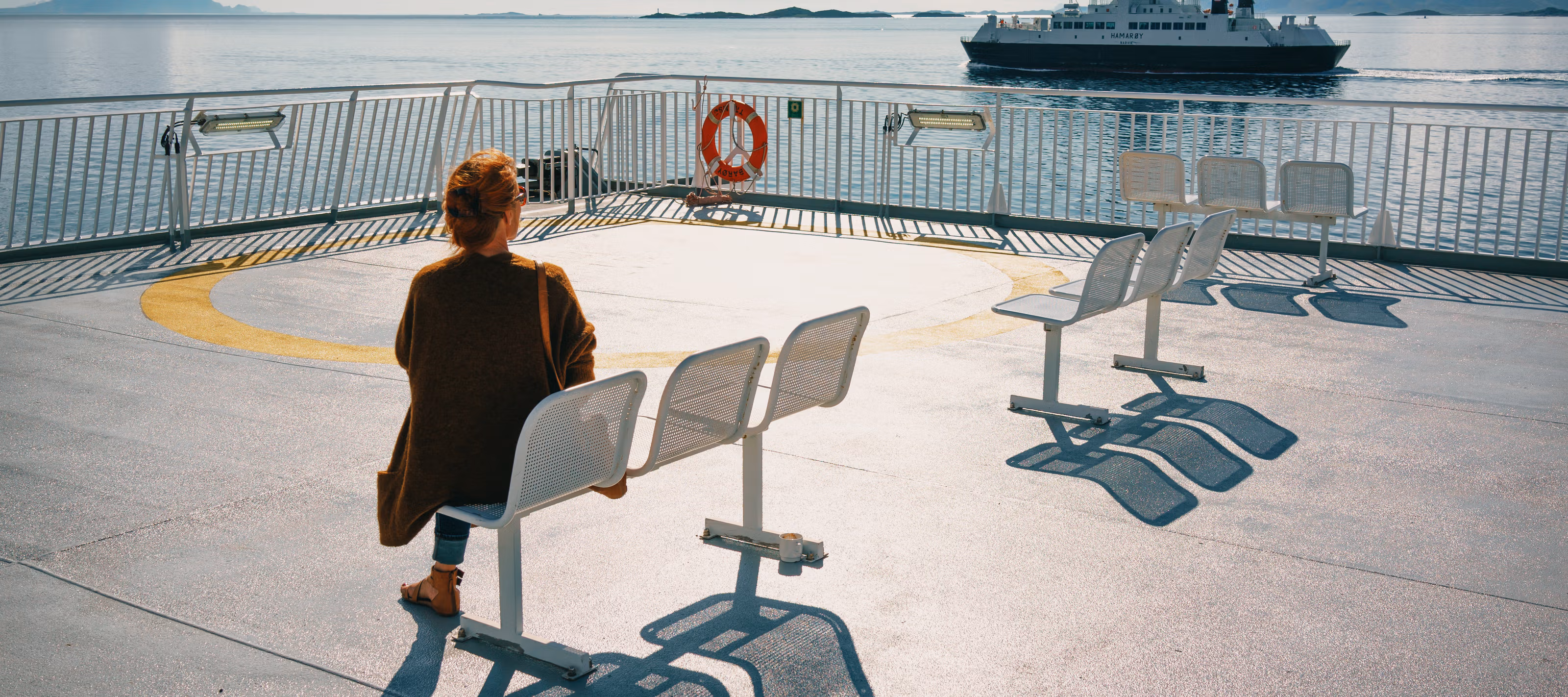 En kvinne sitter på dekk og ser en annen ferge ut på fjorden.