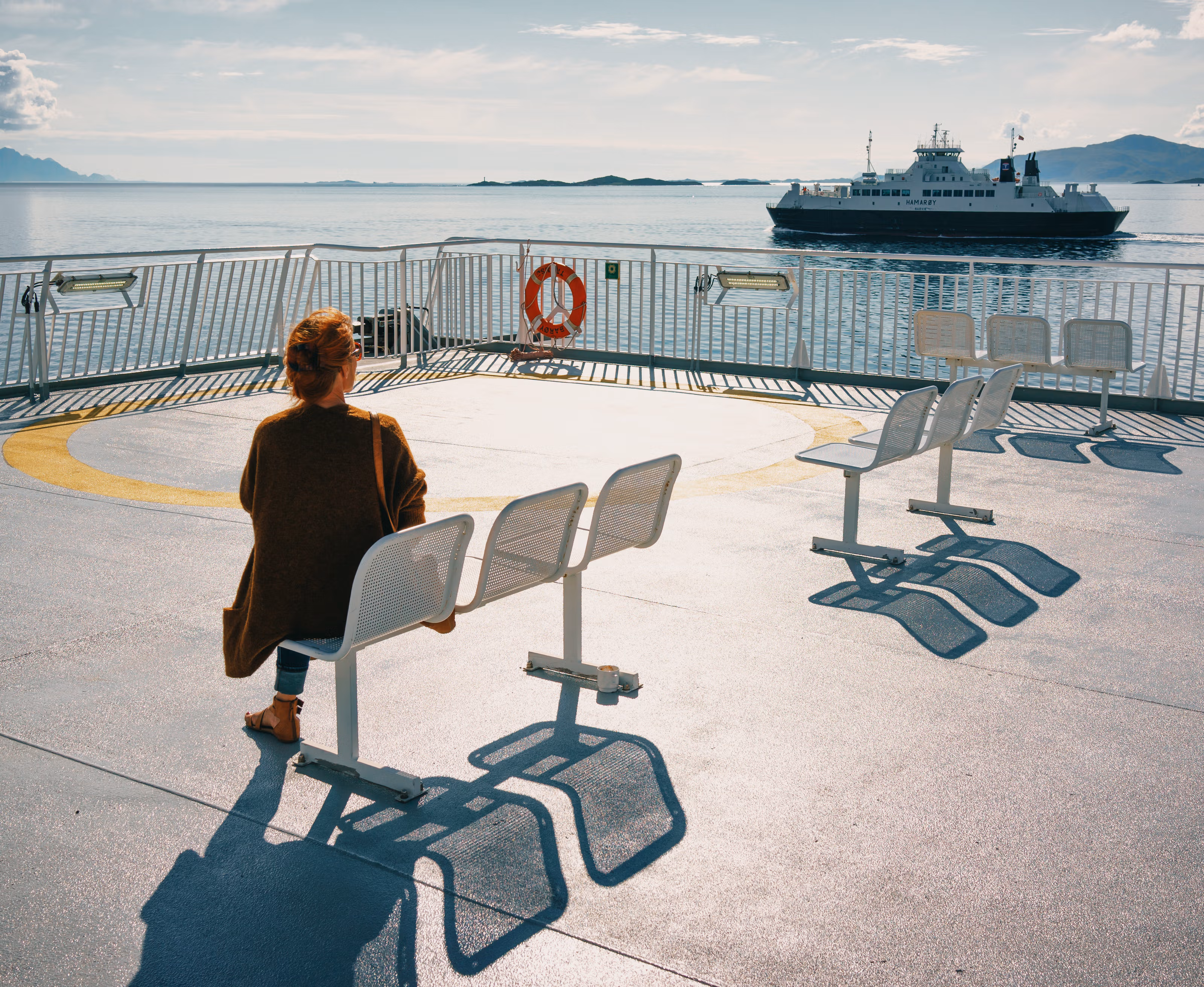 En kvinne sitter på dekk og ser en annen ferge ut på fjorden.
