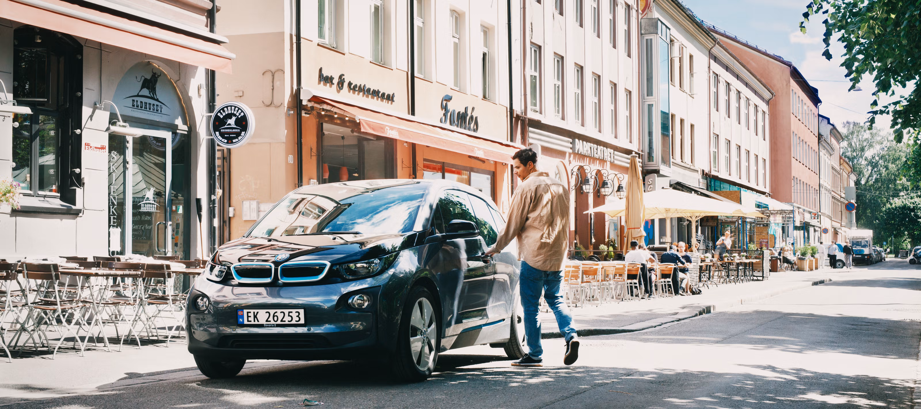 Mann som er i ferd med å åpne døren til en elektrisk bil på Grunerløkka i Oslo en sommerdag.